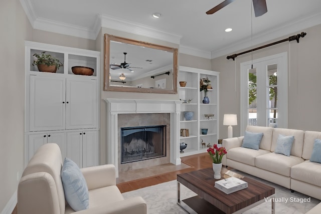 living room featuring ceiling fan, a premium fireplace, light hardwood / wood-style flooring, and crown molding