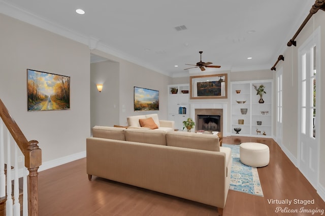 living room with hardwood / wood-style flooring, built in shelves, ceiling fan, a barn door, and ornamental molding