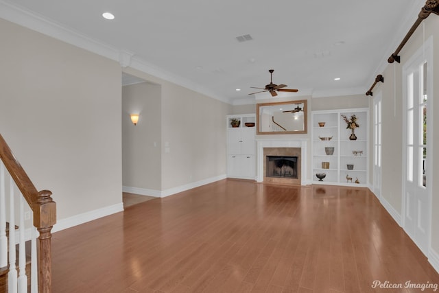 unfurnished living room with hardwood / wood-style floors, crown molding, a barn door, and built in features