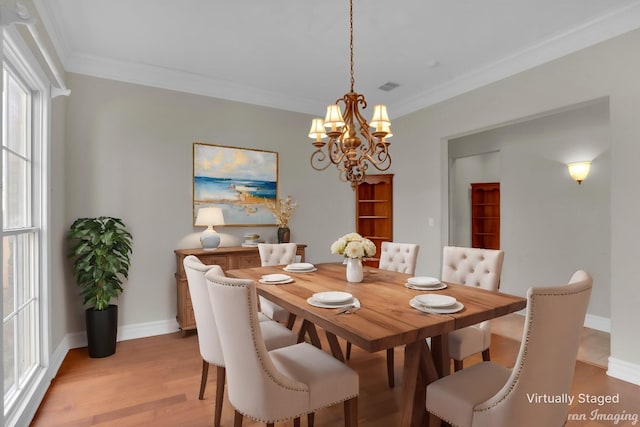 dining area with light wood-type flooring, an inviting chandelier, and crown molding