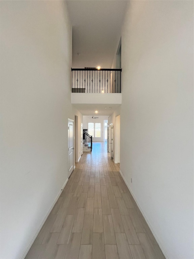 corridor with light wood-type flooring and a towering ceiling