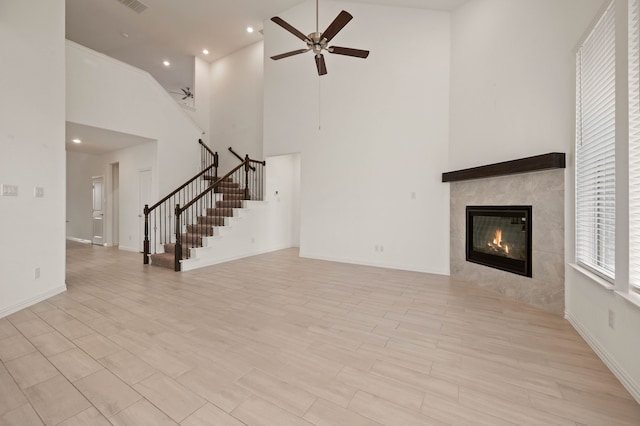 unfurnished living room with ceiling fan, a high ceiling, and a tile fireplace