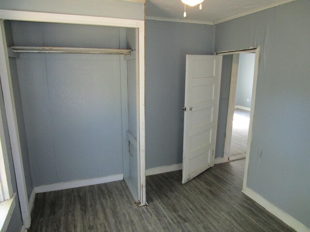 unfurnished bedroom featuring dark wood-type flooring, ornamental molding, and a closet