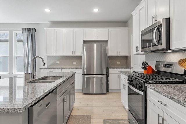 kitchen featuring sink, white cabinets, stainless steel appliances, light stone countertops, and a center island with sink