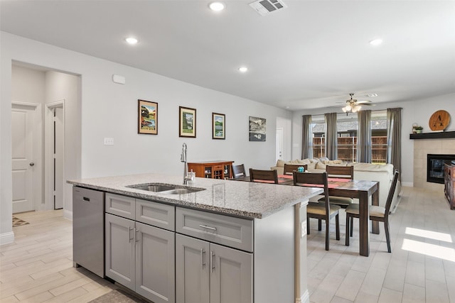 kitchen featuring sink, light stone counters, dishwasher, a tiled fireplace, and a kitchen island with sink