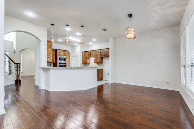 kitchen with kitchen peninsula, light stone countertops, stainless steel appliances, tasteful backsplash, and dark hardwood / wood-style flooring