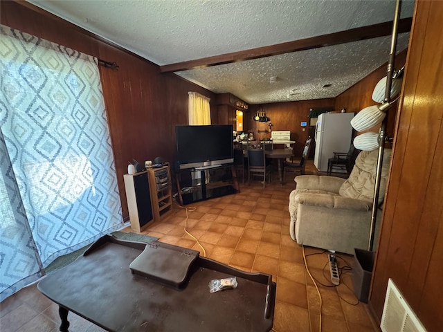 living room with wood walls, a textured ceiling, and beamed ceiling