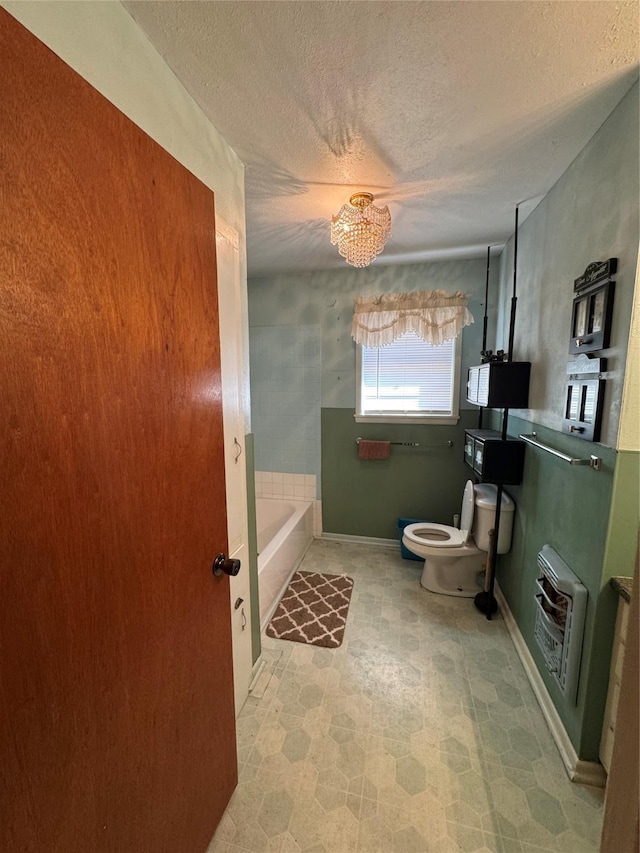 bathroom featuring toilet, a tub, a textured ceiling, a notable chandelier, and heating unit