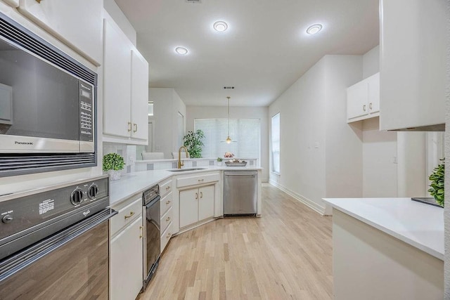 kitchen featuring stainless steel appliances, sink, white cabinets, light wood-type flooring, and pendant lighting