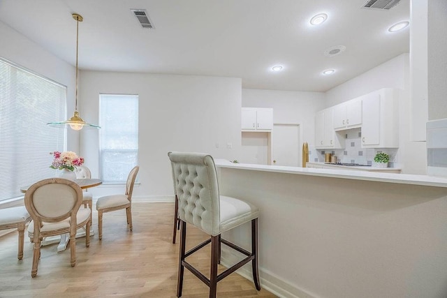 kitchen with light hardwood / wood-style flooring, white cabinets, backsplash, and hanging light fixtures