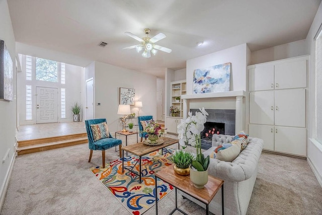 carpeted living room with a tile fireplace, built in features, and ceiling fan