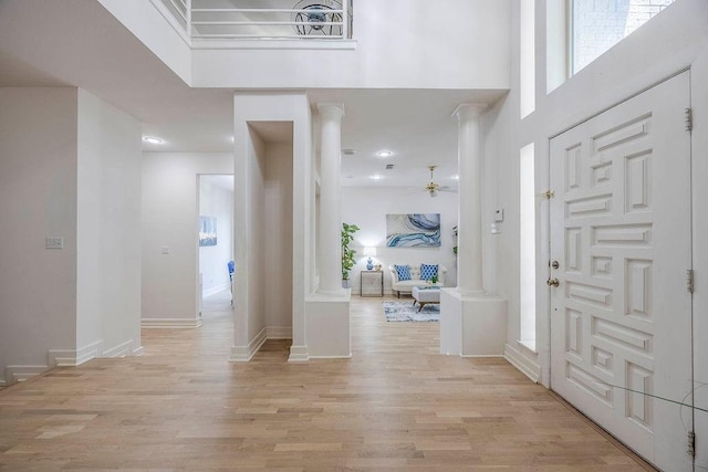 foyer featuring a high ceiling, ceiling fan, light wood-type flooring, and decorative columns