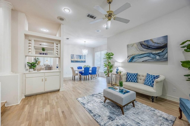 living room with ceiling fan with notable chandelier, built in shelves, and light hardwood / wood-style floors