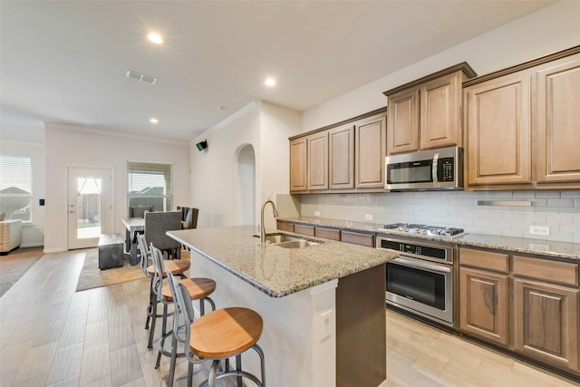 kitchen featuring stainless steel appliances, a kitchen island with sink, and light stone counters