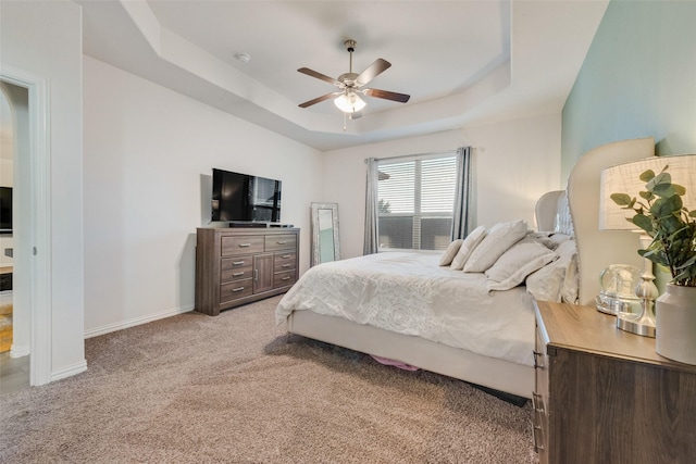 bedroom featuring ceiling fan, a tray ceiling, and light carpet