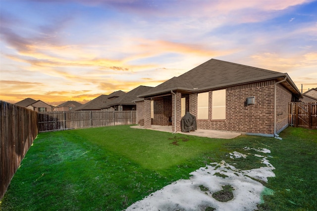 back house at dusk featuring a patio area and a yard