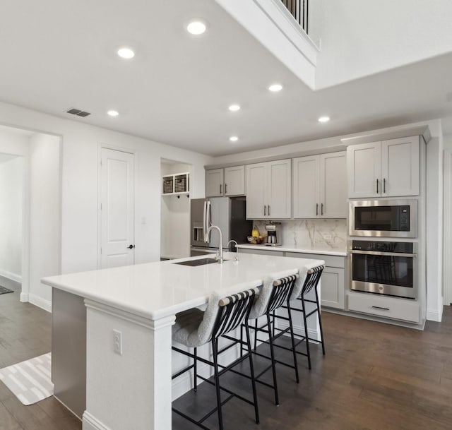 kitchen featuring stainless steel appliances, a large island with sink, dark hardwood / wood-style flooring, a kitchen bar, and sink