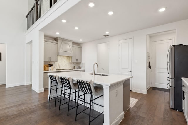 kitchen featuring appliances with stainless steel finishes, dark hardwood / wood-style floors, a center island with sink, and premium range hood