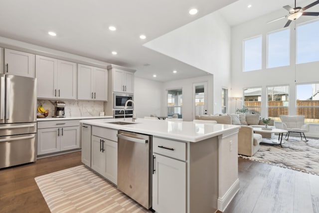 kitchen featuring appliances with stainless steel finishes, an island with sink, hardwood / wood-style flooring, sink, and tasteful backsplash