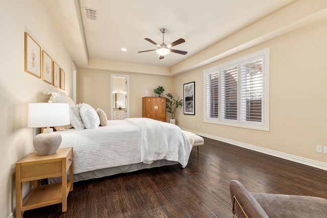 bedroom featuring a raised ceiling, ceiling fan, wood-type flooring, and connected bathroom