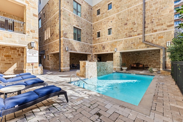 view of swimming pool featuring an outdoor fireplace, pool water feature, and a patio area