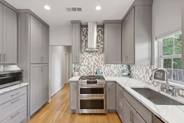 kitchen featuring appliances with stainless steel finishes, gray cabinetry, light stone countertops, wall chimney exhaust hood, and sink