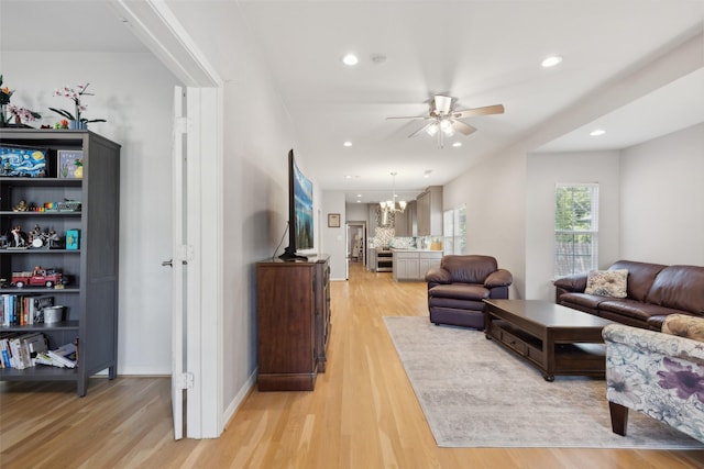 living room featuring ceiling fan with notable chandelier and light hardwood / wood-style floors