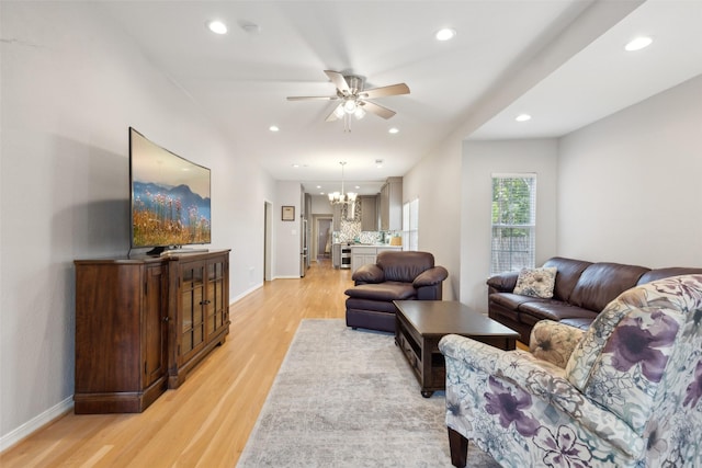 living room featuring ceiling fan with notable chandelier and light hardwood / wood-style flooring