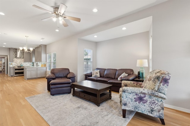 living room with ceiling fan with notable chandelier and light hardwood / wood-style flooring