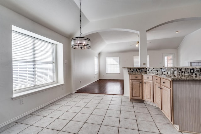 kitchen with vaulted ceiling, light brown cabinets, ceiling fan with notable chandelier, backsplash, and pendant lighting