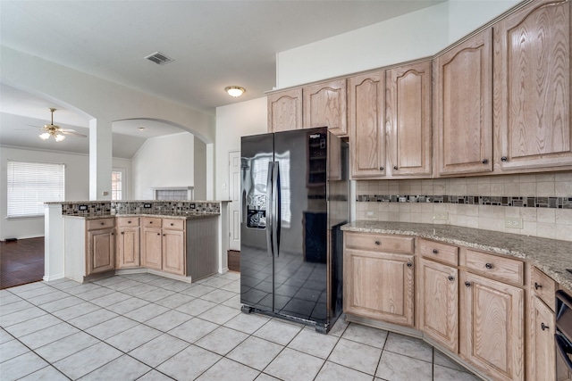 kitchen featuring black refrigerator with ice dispenser, light stone countertops, and light brown cabinetry