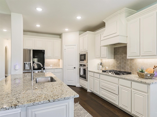 kitchen with appliances with stainless steel finishes, light stone countertops, dark hardwood / wood-style floors, sink, and white cabinetry