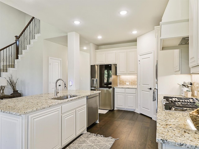 kitchen with custom exhaust hood, white cabinets, appliances with stainless steel finishes, light stone countertops, and sink