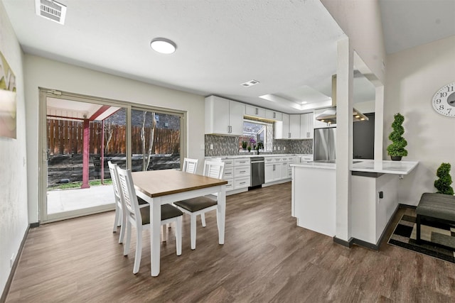 kitchen with kitchen peninsula, stainless steel appliances, tasteful backsplash, dark hardwood / wood-style flooring, and white cabinetry