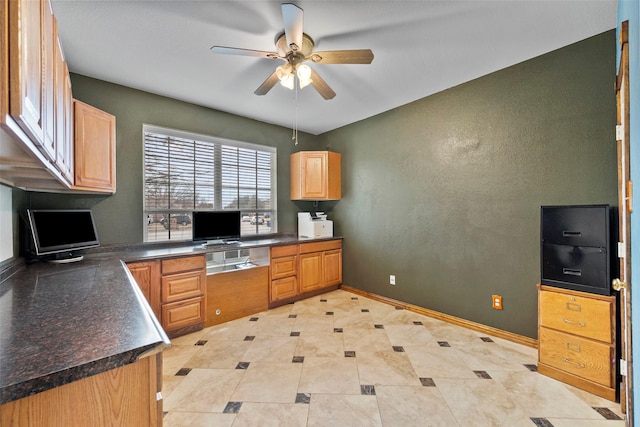 kitchen featuring dark countertops, baseboards, a ceiling fan, and built in study area