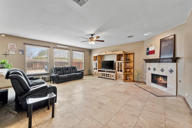 living area with ceiling fan, light tile patterned flooring, a tile fireplace, and visible vents