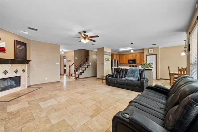 living room featuring baseboards, visible vents, ceiling fan, stairs, and a fireplace