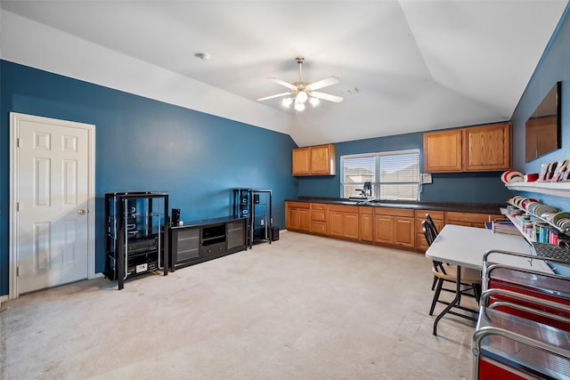 kitchen featuring dark countertops, light colored carpet, brown cabinetry, vaulted ceiling, and ceiling fan