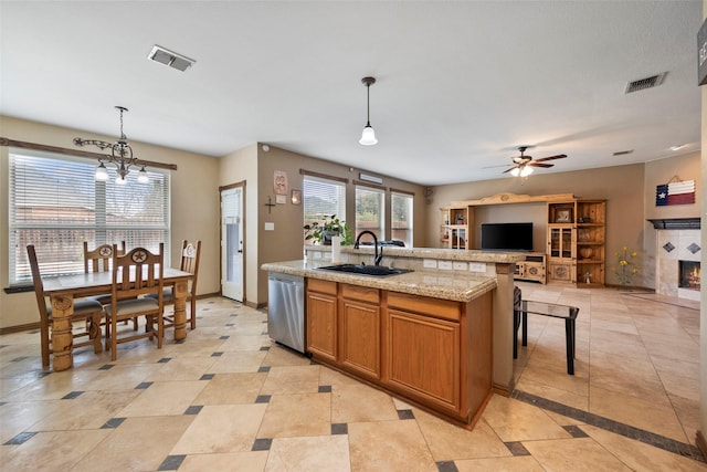 kitchen featuring a fireplace, dishwasher, sink, decorative light fixtures, and an island with sink