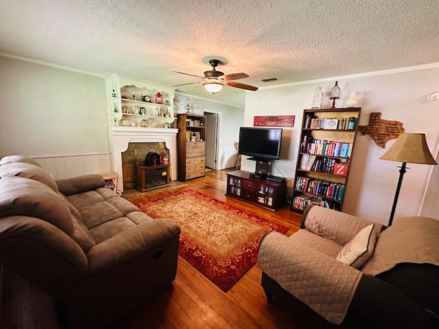 living room with a textured ceiling, a fireplace, ornamental molding, ceiling fan, and hardwood / wood-style flooring