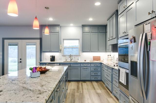 kitchen with light stone counters, gray cabinets, light wood-style floors, a sink, and stainless steel fridge