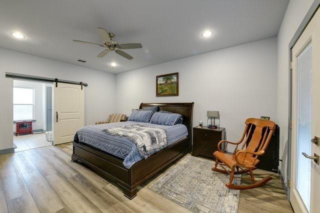 bedroom with light wood-type flooring, a barn door, ceiling fan, and recessed lighting