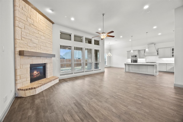 unfurnished living room with ceiling fan with notable chandelier, wood-type flooring, a stone fireplace, and a high ceiling