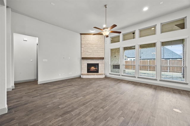 unfurnished living room with a stone fireplace, dark hardwood / wood-style floors, and ceiling fan