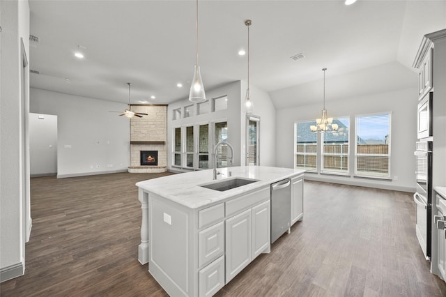 kitchen with a stone fireplace, sink, white cabinets, light stone counters, and a center island with sink