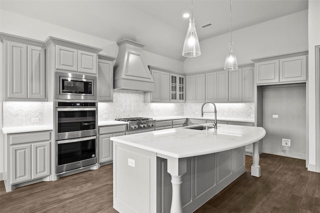 kitchen with sink, dark wood-type flooring, appliances with stainless steel finishes, a center island with sink, and custom exhaust hood