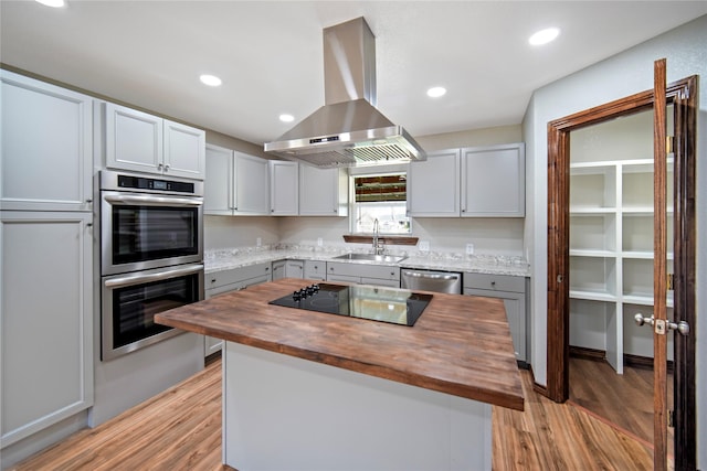 kitchen with island range hood, wood counters, gray cabinetry, appliances with stainless steel finishes, and sink