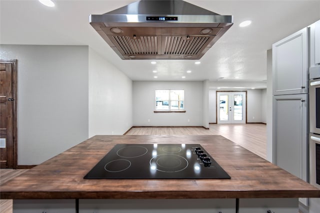 kitchen with island range hood, french doors, light wood-type flooring, black electric stovetop, and butcher block countertops