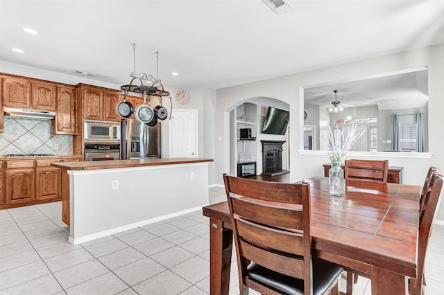 kitchen featuring ceiling fan, a center island, tasteful backsplash, light tile patterned floors, and stainless steel appliances