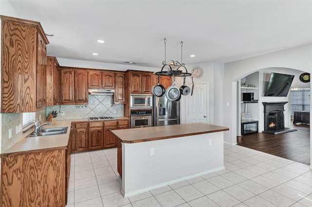 kitchen featuring appliances with stainless steel finishes, a center island, sink, backsplash, and light tile patterned flooring